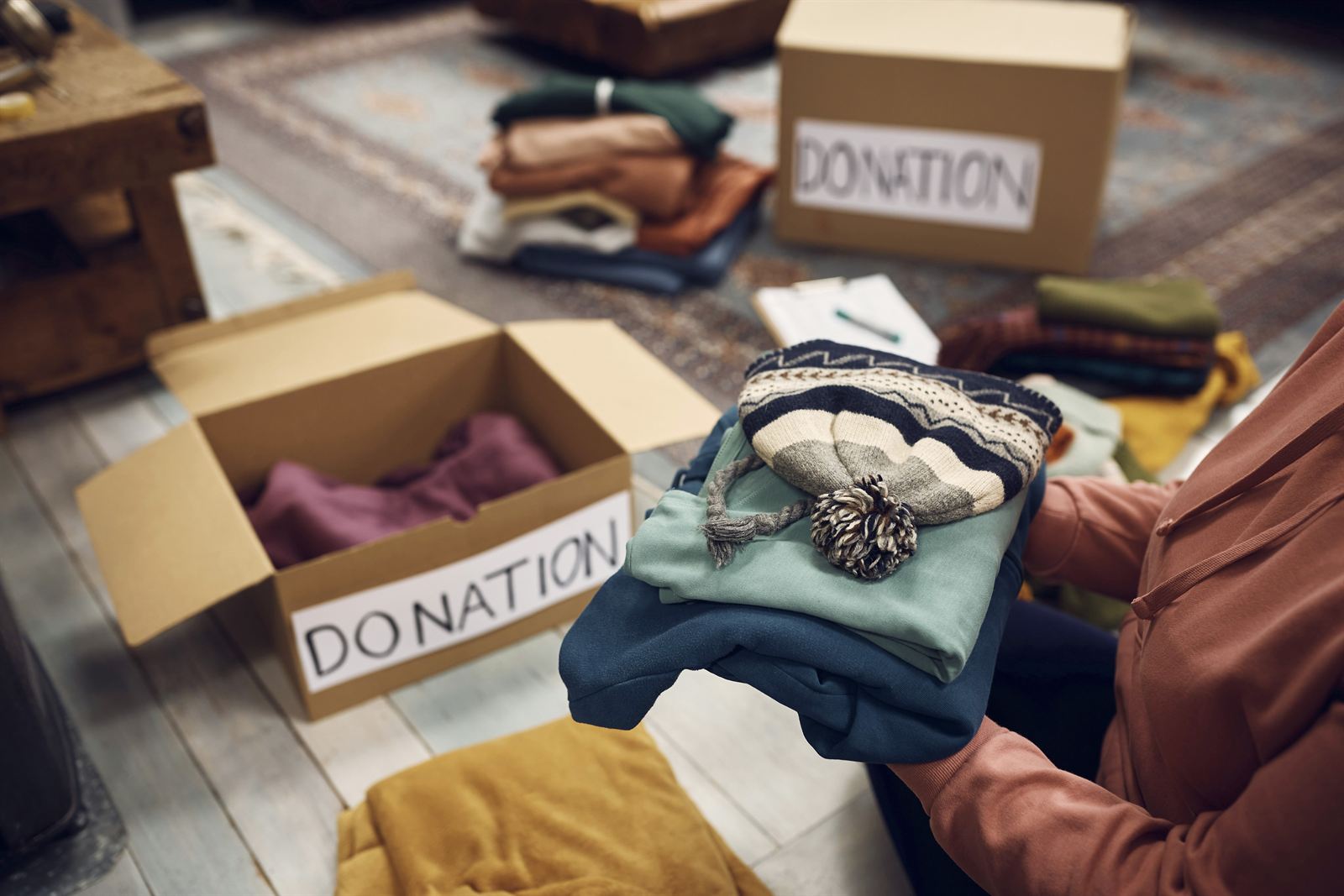 Person sorting clothing into labeled donation boxes while decluttering and organizing belongings at home. Person sorting clothing into labeled donation boxes while decluttering and organizing belongings at home.