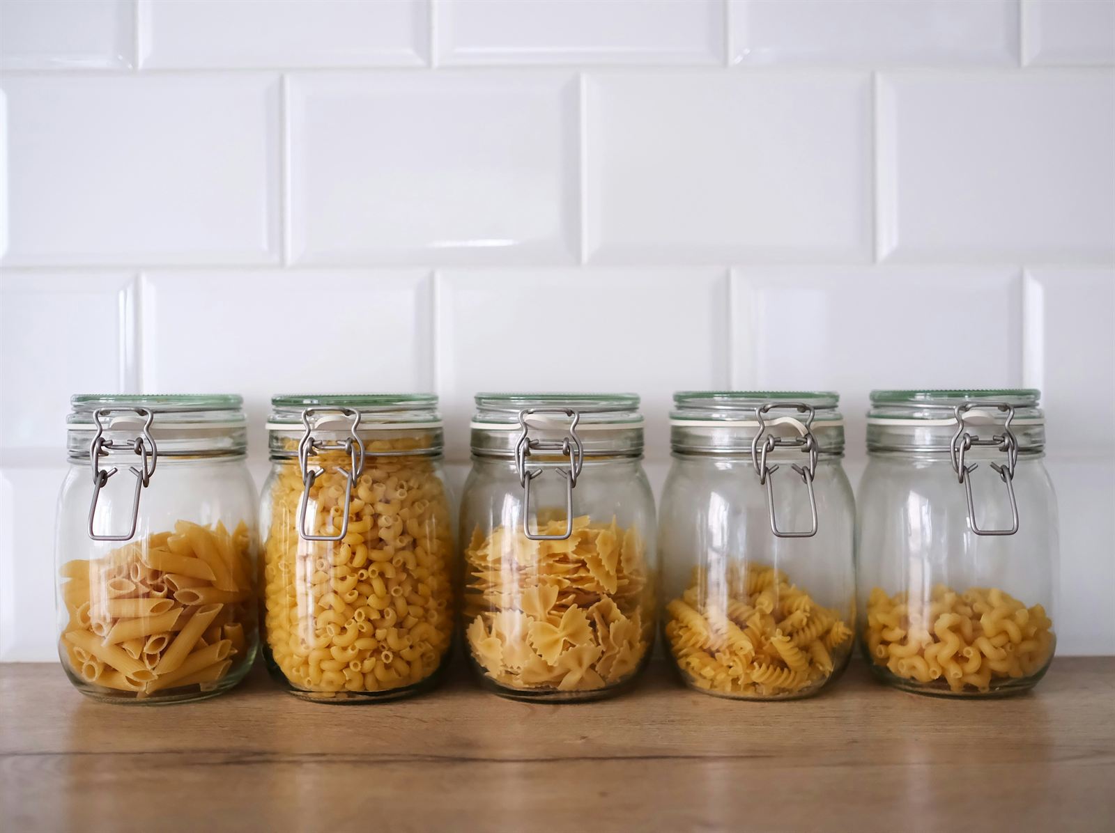 Glass storage jars filled with assorted dry pasta arranged on shelves for simple small kitchen and pantry organization. Glass storage jars filled with assorted dry pasta arranged on shelves for simple small kitchen and pantry organization.