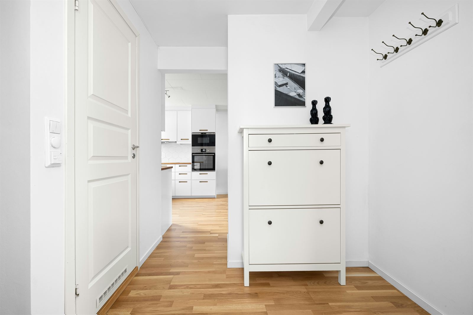 White shoe storage cabinet and wall hooks for space-saving shoe and accessory storage in a small entryway. White shoe storage cabinet and wall hooks for space-saving shoe and accessory storage in a small entryway.