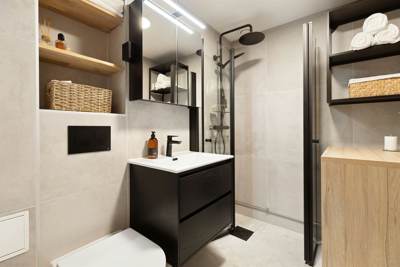 Small modern bathroom with open shelves, woven storage baskets, folded towels, a compact vanity, and a glass shower. Small modern bathroom with open shelves, woven storage baskets, folded towels, a compact vanity, and a glass shower.
